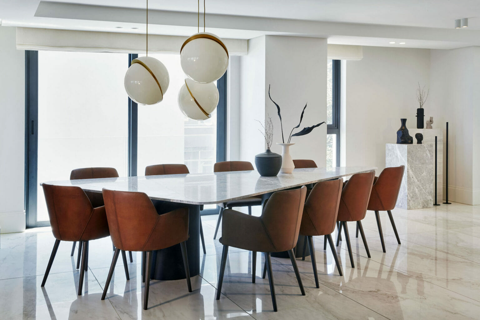 Marble dining room table surrounded by leather chairs underneath unique pendant lights